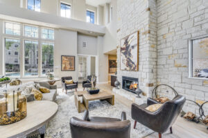 Stylish clubhouse seating area with leather armchairs, a stone fireplace, and large windows providing a scenic outdoor view.