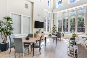 Bright and airy clubhouse dining area with modern tables, chairs, and large windows overlooking the pool area.