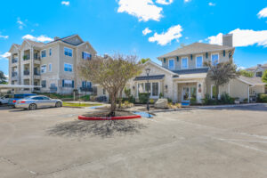 Exterior view of the leasing office at Acclaim at South Congress, showing landscaped surroundings, parking spaces, and nearby apartment buildings.