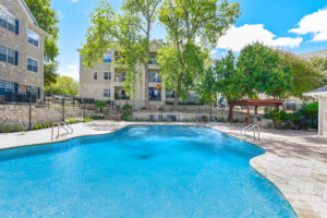 Large resort-style swimming pool surrounded by trees, with apartment buildings in the background at Acclaim at South Congress.