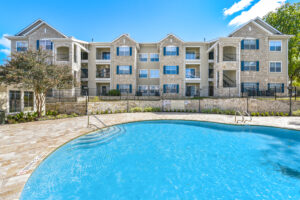 Resort-style swimming pool at Acclaim at South Congress, with a fenced-in pool deck, clear blue water, and apartment buildings in the background.