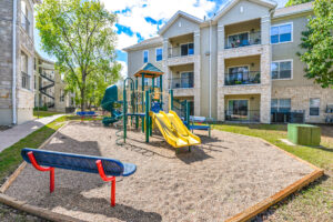 Children's playground area within Acclaim at South Congress, featuring slides, climbing structures, and benches, surrounded by apartment buildings.