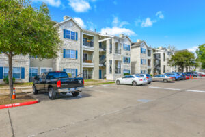 Wide-angle shot of Acclaim at South Congress apartment buildings with a mix of covered and uncovered parking, blue window shutters, and stone exteriors.