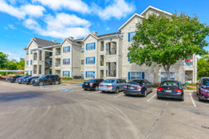 Parking lot of Acclaim at South Congress with multiple vehicles, tree-lined surroundings, and apartment buildings with balconies.