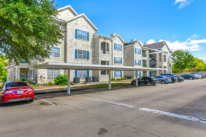 Side view of Acclaim at South Congress buildings, featuring stone exteriors, blue shutters, covered parking, and well-maintained landscaping.