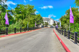 Driveway leading to Acclaim at South Congress with purple flags, lush greenery, and apartment buildings in the background.