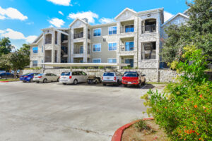 Alternate angle of Acclaim at South Congress apartments, highlighting the balconies, covered parking, and landscaped surroundings with trees and bushes.