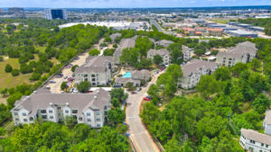 Aerial Exterior wide angle view of Acclaim at South Congress apartment complex, showcasing three-story buildings with stone and stucco exteriors, balconies, and covered parking spaces.