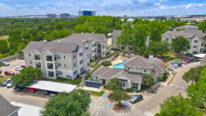 Aerial Exterior wide angle view of Acclaim at South Congress apartment complex, showcasing three-story buildings with stone and stucco exteriors, balconies, and covered parking spaces.