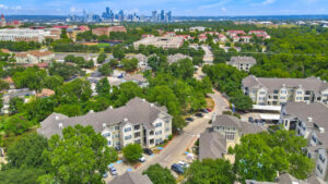 Aerial Exterior wide angle view of Acclaim at South Congress apartment complex, showcasing three-story buildings with stone and stucco exteriors, balconies, and covered parking spaces.