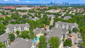 Aerial Exterior wide angle view of Acclaim at South Congress apartment complex, showcasing three-story buildings with stone and stucco exteriors, balconies, and covered parking spaces.