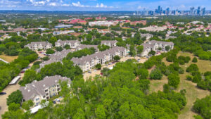 Aerial Exterior wide angle view of Acclaim at South Congress apartment complex, showcasing three-story buildings with stone and stucco exteriors, balconies, and covered parking spaces.