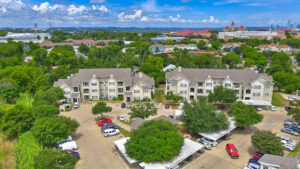 Aerial Exterior wide angle view of Acclaim at South Congress apartment complex, showcasing three-story buildings with stone and stucco exteriors, balconies, and covered parking spaces.