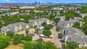 Aerial Exterior wide angle view of Acclaim at South Congress apartment complex, showcasing three-story buildings with stone and stucco exteriors, balconies, and covered parking spaces.
