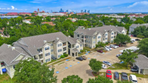 Aerial Exterior wide angle view of Acclaim at South Congress apartment complex, showcasing three-story buildings with stone and stucco exteriors, balconies, and covered parking spaces.