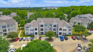 Aerial Exterior Front view of Acclaim at South Congress apartment complex, showcasing three-story buildings with stone and stucco exteriors, balconies, and covered parking spaces.