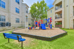 Children's playground area within Acclaim at South Congress, featuring slides, climbing structures, and benches, surrounded by apartment buildings.