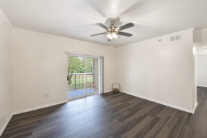 Spacious living area with a ceiling fan, wood-style flooring, and sliding glass doors leading to a private balcony.