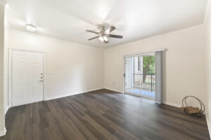 Spacious living area with a ceiling fan, wood-style flooring, and sliding glass doors leading to a private balcony.