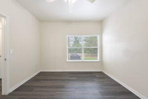 Bedroom with large window, neutral walls, wood-style flooring, and a ceiling fan.
