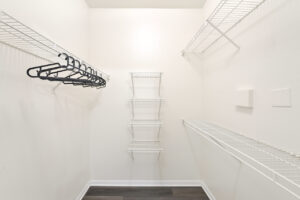 Spacious walk-in closet with white wire shelving and dark wood-style flooring.