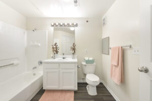 Modern bathroom with a white vanity, bright lighting, bathtub, and soft pink towel accents.