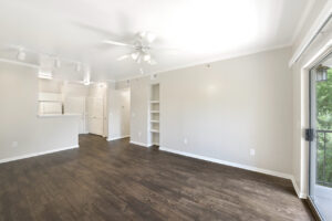 Modernized living area with dark wood-style flooring, white walls, built-in shelves, and a balcony.