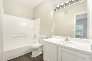 Bathroom with a large vanity, mirror with bright lighting, bathtub, and white fixtures.