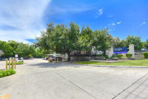 Exterior view of the Acclaim at South Congress apartment complex with a large tree, parking area, and security gate.