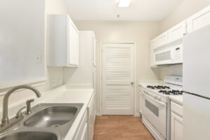 Galley-style kitchen with white appliances, solid surface countertops, and white cabinetry.